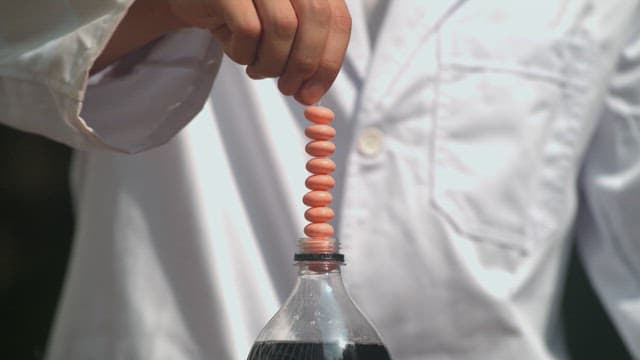 Scientist demonstrating a reaction by dropping candies into a soda, resulting in a foam eruption