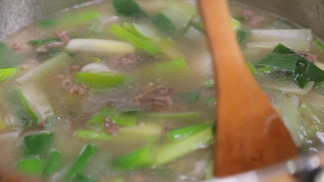 Soup dish with green onions and beef being stirred with a wooden spatula