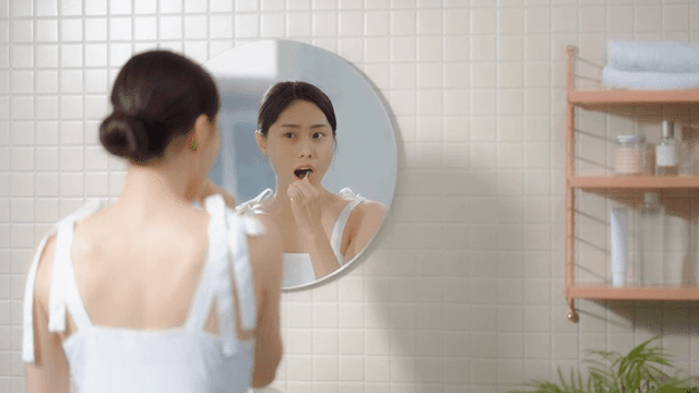 Woman brushing teeth in front of the mirror in the bathroom