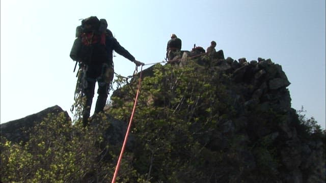 Climbers climbing a mountain peak while holding a rope