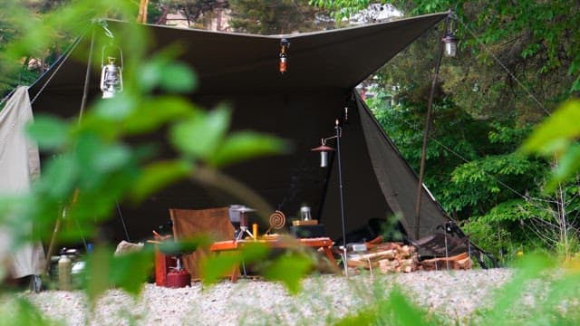 Tents and camping equipment prepared on a gravel field surrounded by green bushes