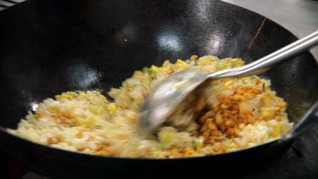 Stir-frying rice with vegetables and eggs in a wok