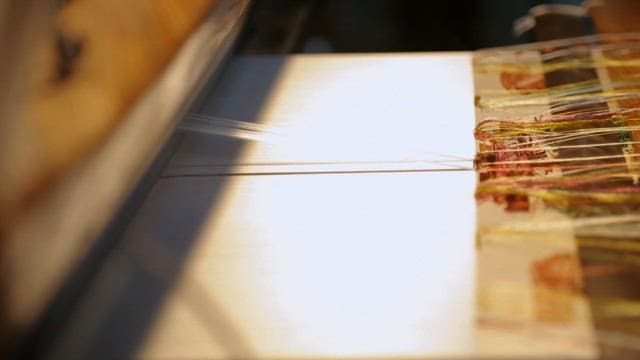 Skilled hand weaving intricate patterns with colorful threads in a traditional loom