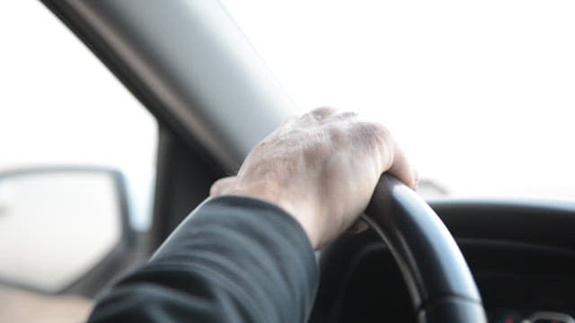 Person driving a car with a focus on the hands gripping the steering wheel