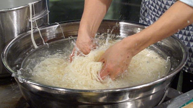 Hands washing noodles in a large bowl