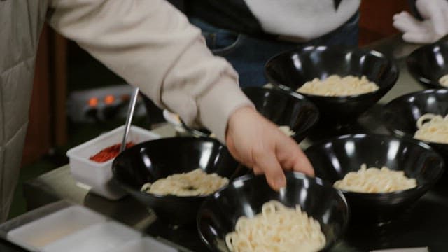 Pouring broth into a bowl containing udon noodles with a ladle