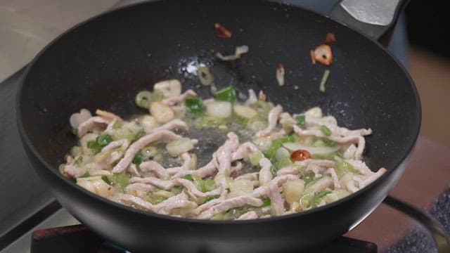 Cooking pork strips with vegetables in a frying pan