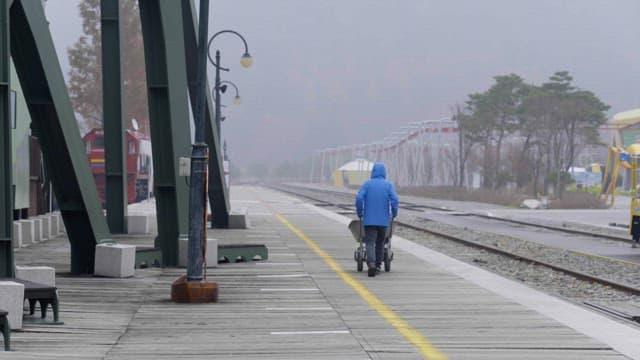 Person in a blue jacket pushing a cart on a foggy railway platform