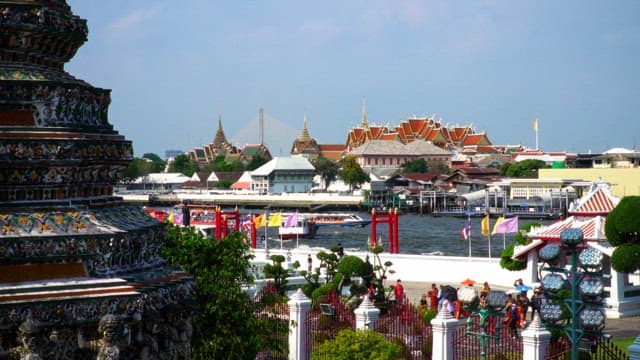 Tourists exploring a waterfront temple with passing boats on a sunny day