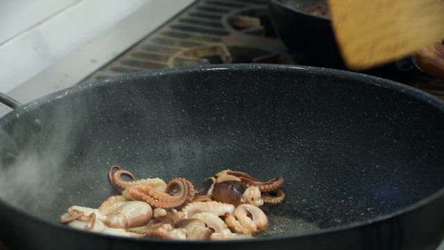 Webfoot octopus being stir-fried with spicy seasoning in a pan