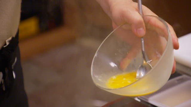 Hand stirring egg mixture into boiling soup on a stove