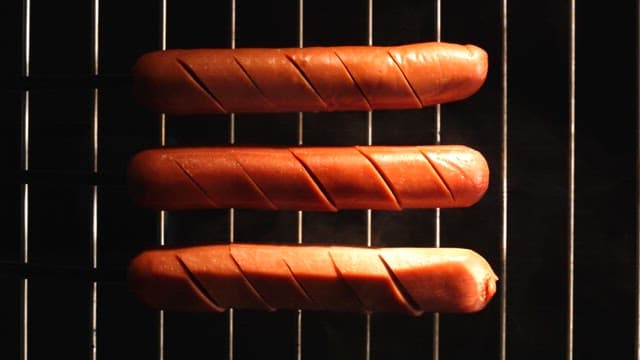 Three sausages grilling with smoke rising