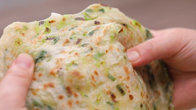 Hands tearing a green onion pancake