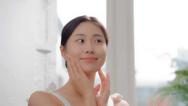 Woman smiling and touching her face in a bright room