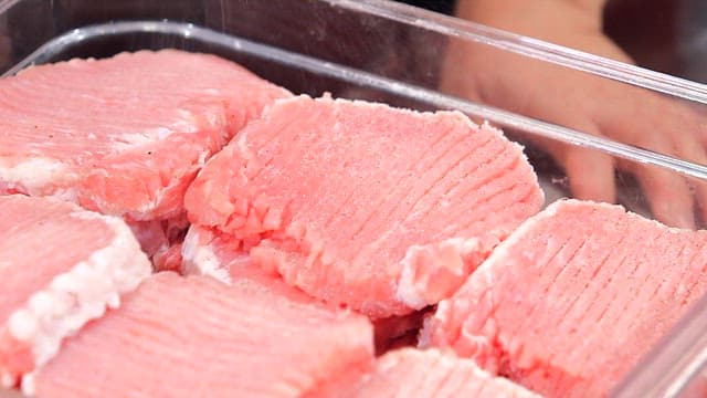 Sprinkling pepper on freshly cut pork slices in a container
