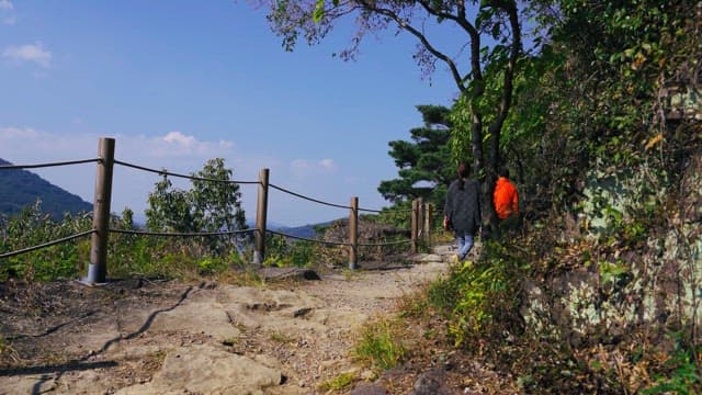 Two people hiking a mountain path on a sunny day
