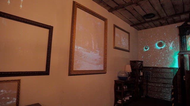 A room adorned with clocks and paintings, featuring forest and space-themed projections.