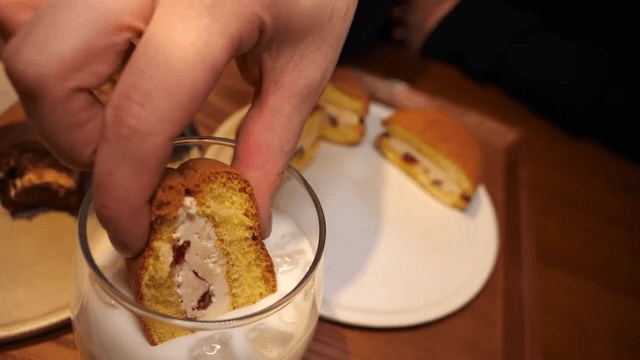 Person dipping a cream-filled bun into a glass of milk.