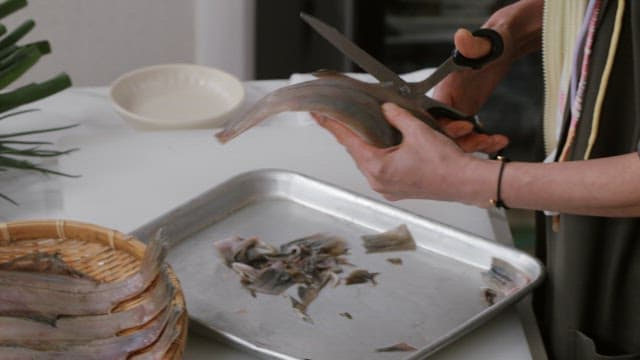 Person preparing and cleaning fish with scissors in a kitchen