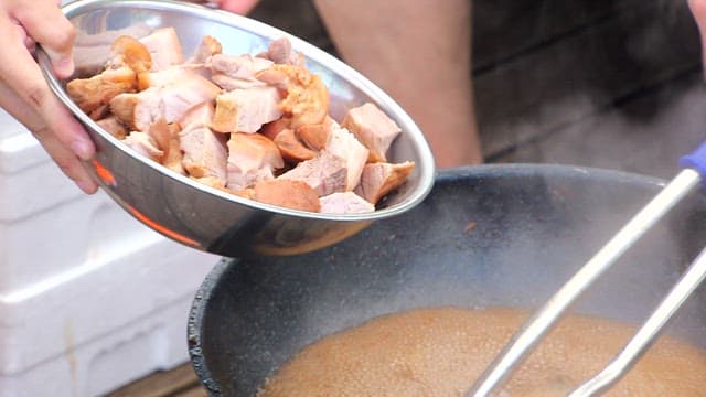 Pork being added to a pot with simmering soy sauce