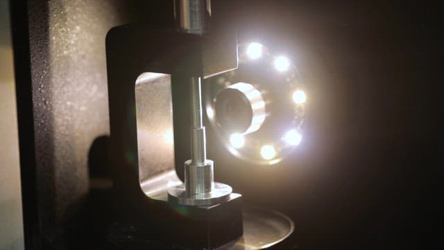 Precision tool working on a pink gemstone under bright lights