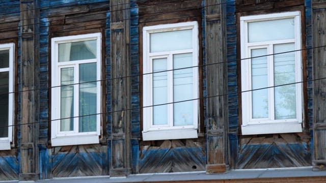 Close-up view of old wooden building facade with peeling blue paint and white framed windows