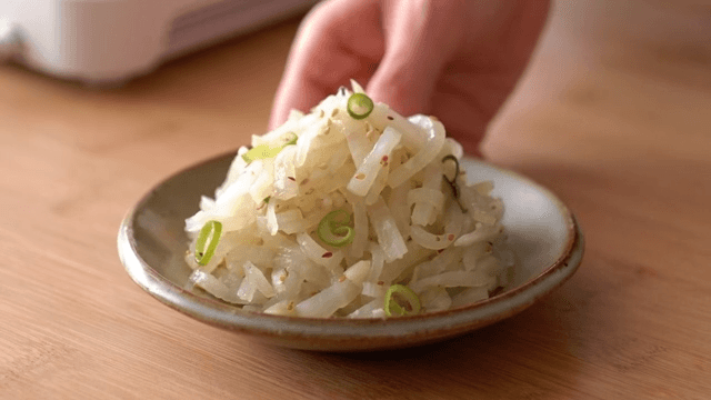 Hand placing a bowl of radish salad on a wooden table