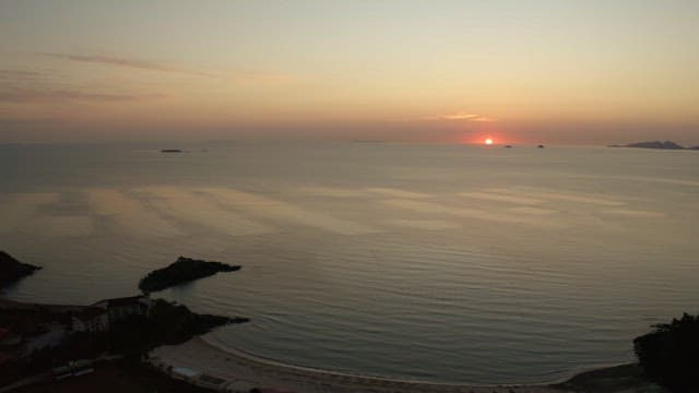 Sunset over a calm sea with distant islands and coastal buildings
