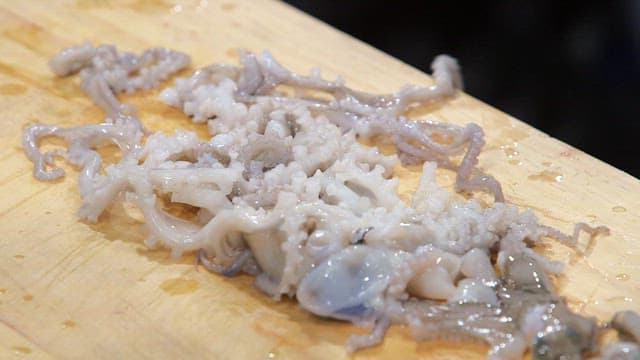 Live octopus being cut with a knife on a wooden cutting board