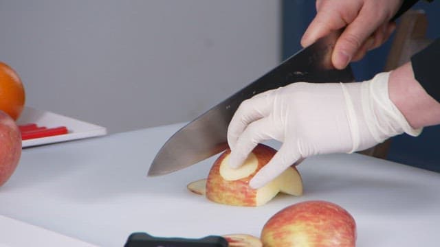 Gloved hand slicing an apple on a cutting board