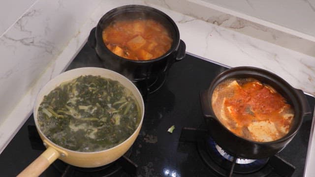 Various soups boiling on a stove in a kitchen