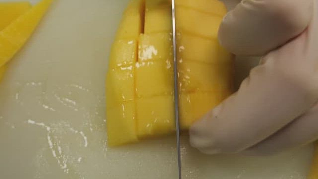 Hands slicing ripe yellow mango on white cutting board.