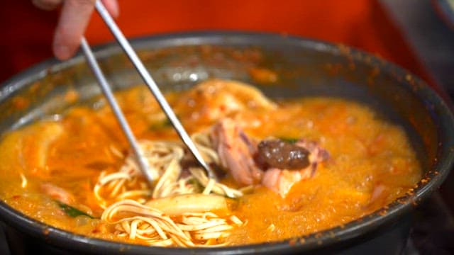 Noodles picked from the spicy noodle soup with chicken boiling in the pot