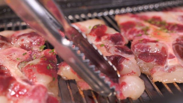Grilling juicy meat with tongs on a hot grill
