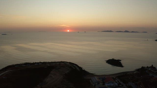 Sunset over a calm sea with distant islands and coastal buildings