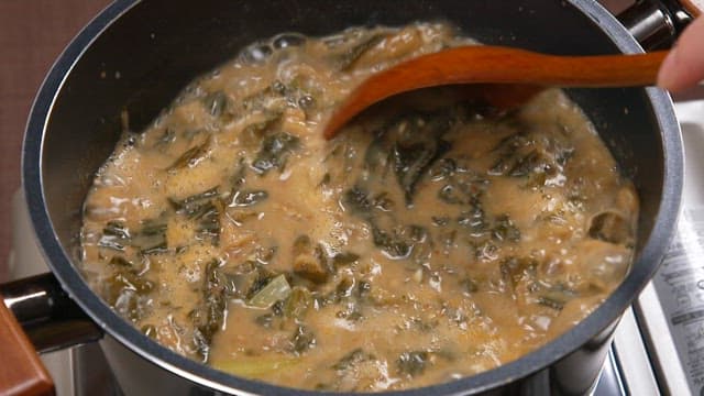 Stirring the savory chueotang with dried radish greens with a wooden spatula