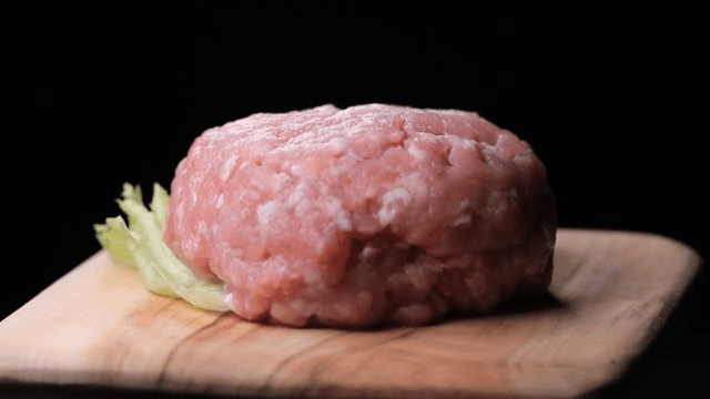 Raw pork patty on a wooden board
