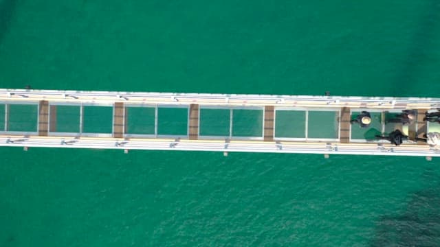 Tourists Walking Across a Glass Bridge over the River on a Sunny Day