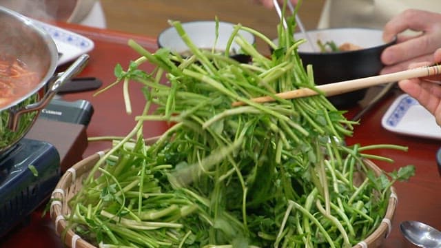Fresh water parsley going into a boiling hot pot in a pot