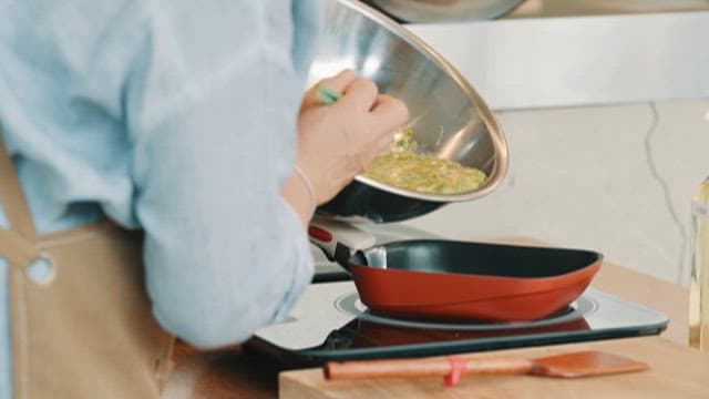 Person Pouring Egg Mixture into a Frying Pan on a Stovetop