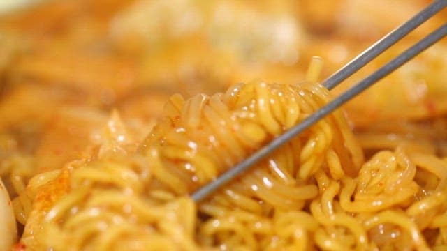 Chopstickful of glossy noodle in spicy tteokbokki with ramen