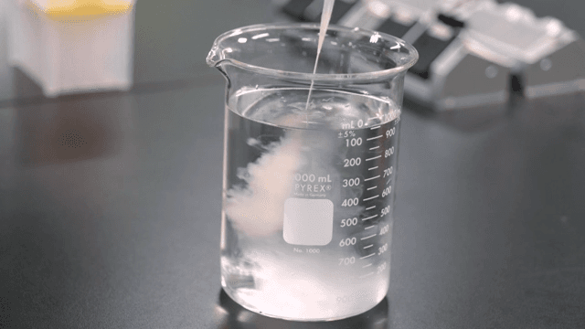 Yellow liquid poured into a beaker of water on a laboratory table using a dropper