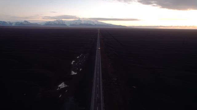 Car driving on a long road under a sunset sky