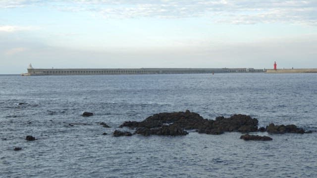 Calm sea with a long breakwater visible in the distance