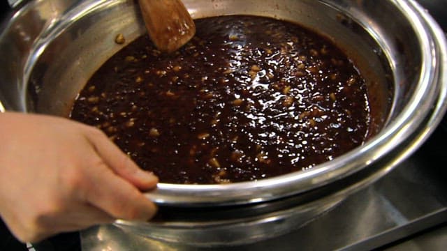Stirring a pot of sauce made with chestnuts and red beans with a wooden spoon