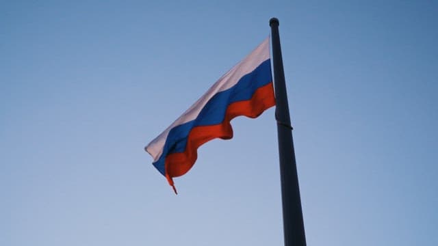 Waving national Russian flag on a tall flagpole against a clear sky