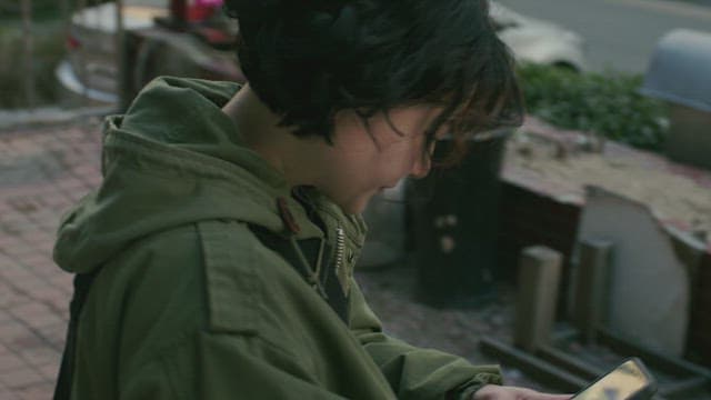 Person in a green jacket holding a cell phone and talking on the phone on the street