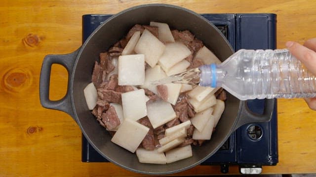 Pouring water into the pot where the beef broth is being cooked