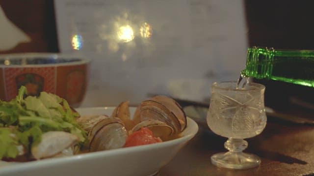 Soju poured into a glass next to steamed clams on the table