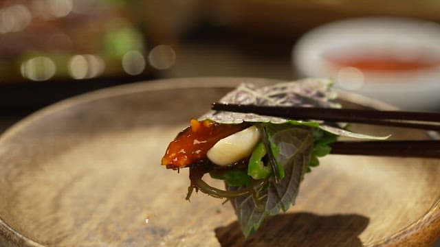 Picking up perilla leaf with ssamjang and garlic with chopsticks